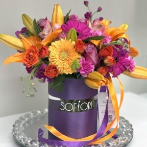 Vibrant summer floral bouquet in a sleek purple Sofiori vase, featuring a mix of orange lilies, pink carnations, yellow chrysanthemums, and purple asters.